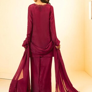 May include: A burgundy-colored outfit with a long-sleeved top and wide-legged pants. The top has a delicate lace trim around the neckline. The outfit is paired with a matching sheer dupatta with lace trim.