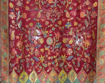 May include: A richly coloured red textile featuring detailed floral designs in yellow, orange, green, and blue. The textile has a floral border and a diamond-shaped pattern at the bottom. Ideal for home decor or fashion applications.