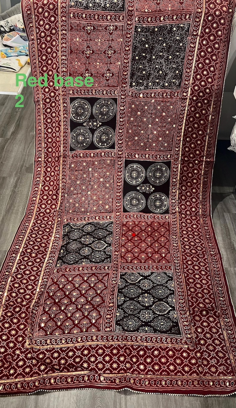 K&ouml;nnte beinhalten: Burgunderfarbenes Textil mit Patchwork-Design. Das Textil weist verschiedene Muster auf, darunter geometrische Formen, florale Motive und kreisf&ouml;rmige Designs. Goldfarbene Verzierungen und Bord&uuml;ren sorgen f&uuml;r Details. Der Text "Red base 2" ist sichtbar.