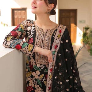 May include: Black embroidered tunic and matching scarf. The tunic features floral embroidery in red, green, and gold. The scarf has a delicate pattern and gold embellishments. The outfit is a traditional style.
