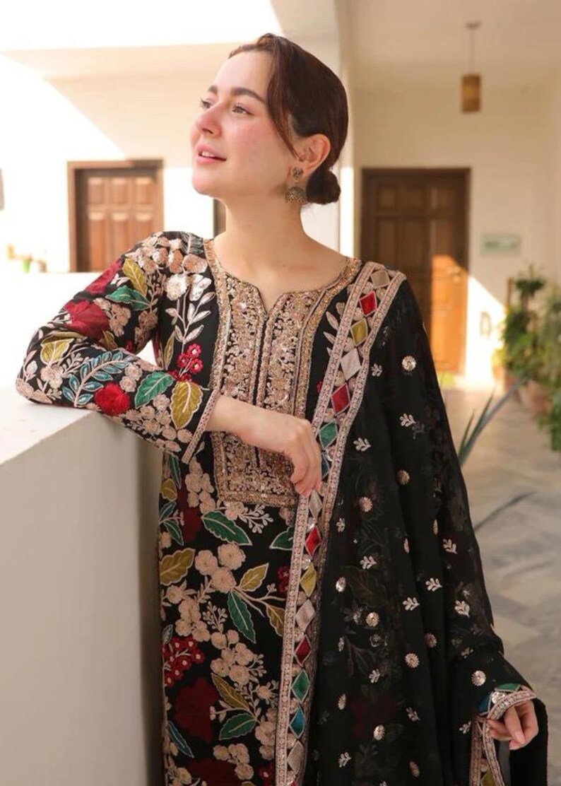 May include: Black embroidered tunic and matching scarf. The tunic features floral embroidery in red, green, and gold. The scarf has a delicate pattern and gold embellishments. The outfit is a traditional style.