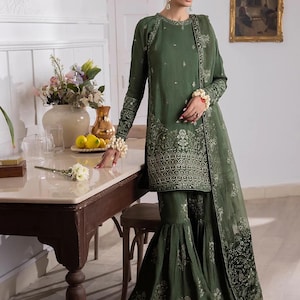May include: A green embroidered dress with a long-sleeved top and a flared bottom. The dress has a floral pattern and is paired with a sheer dupatta.