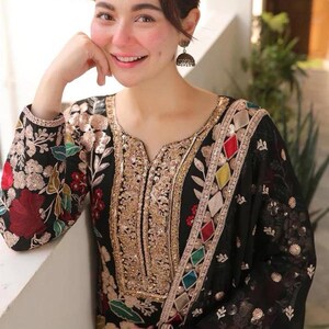 May include: Black embroidered tunic with gold sequin detailing and colorful geometric accents. The long-sleeved garment features floral embroidery in red, green, and gold. The neckline and borders are embellished with gold sequins.