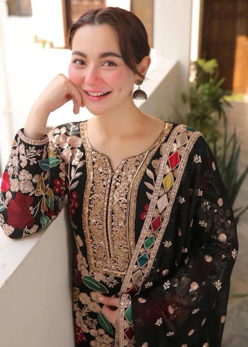 May include: Black embroidered tunic with gold sequin detailing and colorful geometric accents. The long-sleeved garment features floral embroidery in red, green, and gold. The neckline and borders are embellished with gold sequins.