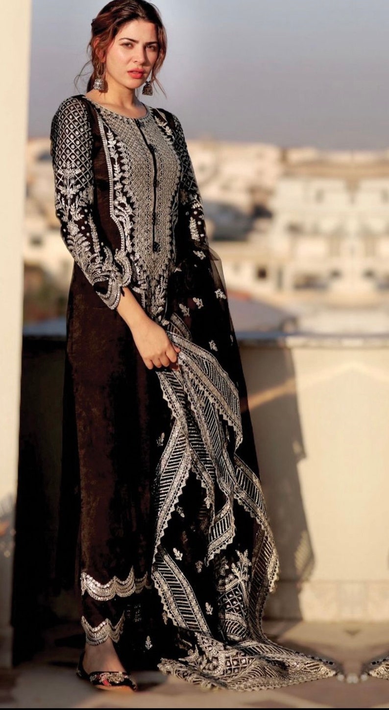 May include: A black and silver embroidered dress with a long, flowing skirt and a sheer, embroidered dupatta. The dress has a high neckline and long sleeves. The embroidery is intricate and detailed, and the dress is perfect for a special occasion.