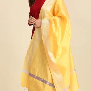 May include: A yellow dupatta with a silver border and small white dots. The dupatta is draped over a woman wearing a maroon long-sleeved top.