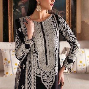 May include: A black long-sleeved dress with silver embroidery. The dress has a round neckline and a long skirt. The model is wearing a silver headpiece and earrings.