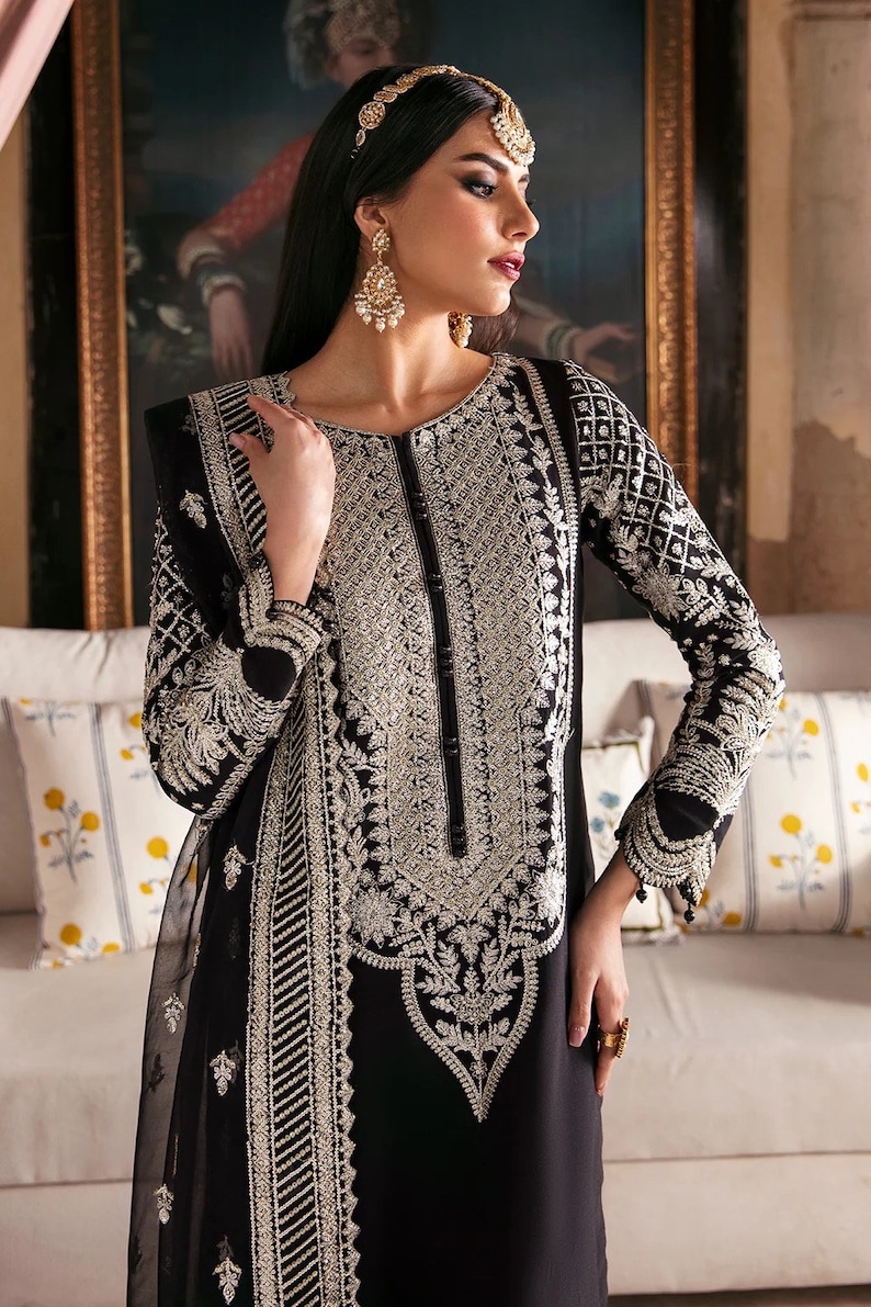 May include: A black long-sleeved dress with silver embroidery. The dress has a round neckline and a long skirt. The model is wearing a silver headpiece and earrings.