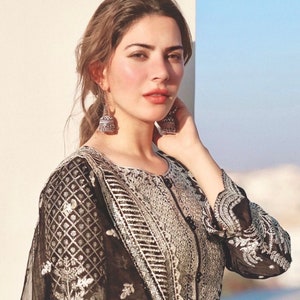 May include: A woman with long brown hair wearing a black and silver embroidered dress with a silver pendant earring on each ear.