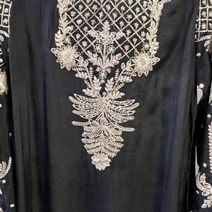 May include: A black long-sleeved tunic with silver embroidery featuring a floral design. The embroidery is intricate and detailed, with a geometric pattern at the neckline.