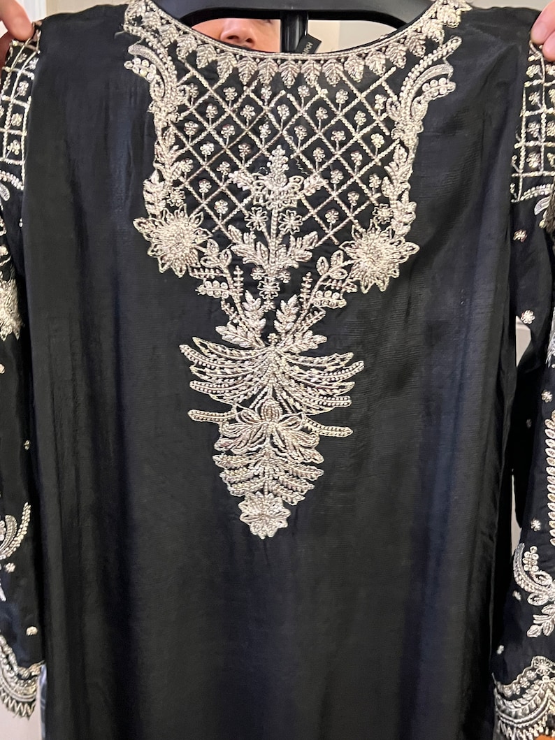 May include: A black long-sleeved tunic with silver embroidery featuring a floral design. The embroidery is intricate and detailed, with a geometric pattern at the neckline.