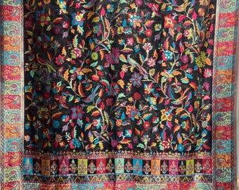 May include: Black shawl with a colourful floral and bird pattern in red, blue, green, and orange. The border features a detailed paisley design. The shawl has a fringed edge.