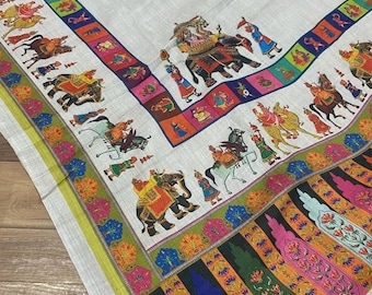 May include: A white fabric with a colourful border featuring a procession of elephants, horses, and people. The border is made up of repeating patterns of flowers and geometric shapes.