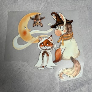 Könnte beinhalten: Eine fantasievolle Illustration eines weißen Pferdes mit Hexenhut und Brille, eines Fuchses in einem weißen Gewand mit Zauberstab und einer Fledermaus, die kopfüber an einem Halbmond hängt. Die Illustration ist im Cartoon-Stil mit sanften Farben gehalten.