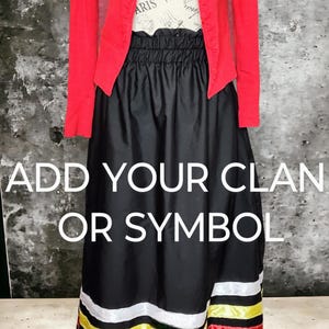 May include: A black skirt with a red, white, and yellow striped trim. The skirt has an elastic waistband and is made of a soft, flowing fabric. The text "ADD YOUR CLAN OR SYMBOL" is printed on the skirt.