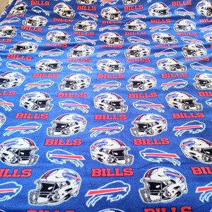 May include: A blue fleece blanket with a repeating pattern of white football helmets and red "BILLS" text. The blanket has a white sherpa lining.