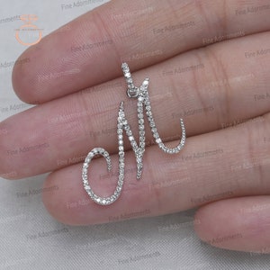 May include: A diamond pendant in the shape of the letter M. The pendant is made of white gold and is set with small, round diamonds.