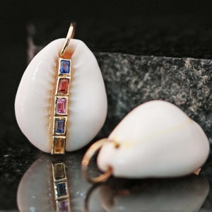 May include: A white seashell pendant with a gold chain and a row of colourful gemstones. The gemstones are red, pink, blue, and yellow.