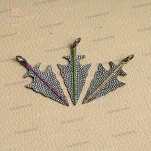 May include: Three silver arrowhead pendants with pave diamond settings and a single line of colorful gemstones. The pendants are on a brown background.