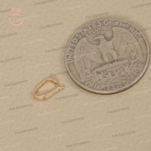 May include: A gold-colored clasp with a row of small, clear gemstones. The clasp is next to a US quarter coin for size comparison. The clasp is a jewelry component, likely for a necklace or bracelet.