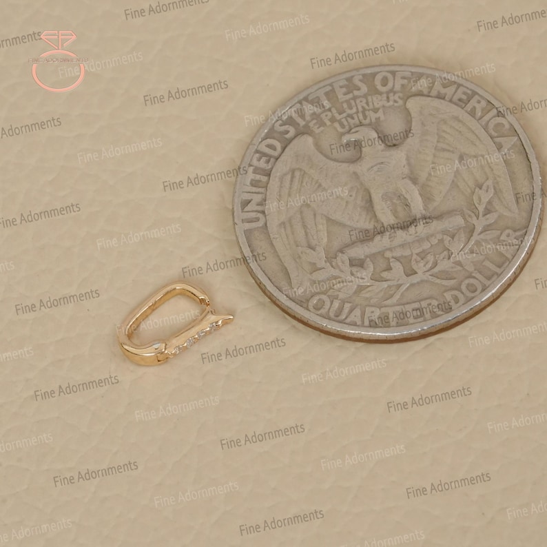 May include: A gold-colored clasp with a row of small, clear gemstones. The clasp is next to a US quarter coin for size comparison. The clasp is a jewelry component, likely for a necklace or bracelet.