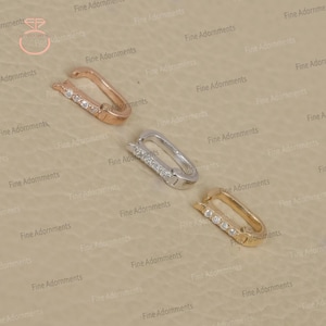 May include: Three rectangular jewelry clasps in rose gold, silver, and gold. Each clasp features a row of small, clear gemstones. The clasps are displayed on a neutral, textured surface.