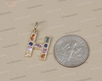 以下が含まれることがあります： 金属にカラフルな宝石が埋め込まれた、Hの字型の金のチャーム。チャームは、大きさの比較のためにアメリカ合衆国の10セント硬貨の隣に置かれています。