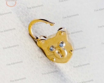 May include: A gold-colored bear charm with a keyhole and two small clear stones for eyes. The charm is attached to a gold-colored loop.