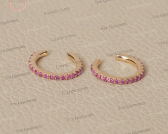 May include: A pair of gold ear cuffs with pink gemstones. The cuffs are designed to sit on the upper part of the ear, without piercing.