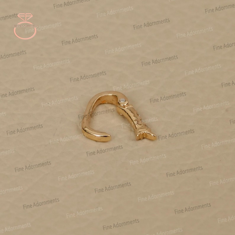 May include: A gold-colored nose ring with a curved design and a small decorative element. The nose ring is made of metal and has a smooth, polished finish. The jewelry is designed to be worn in the nose.
