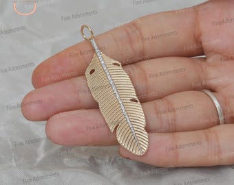 May include: A gold feather pendant with a row of clear diamonds down the center. The pendant is on a gold chain.