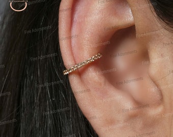 May include: A gold ear cuff with small clear stones set in a circular design. The cuff is worn on the upper part of the ear.