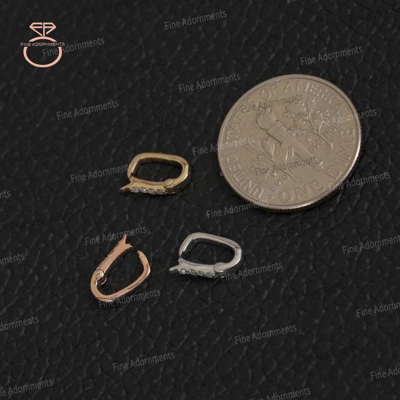 May include: Three small jewelry clasps in gold, rose gold, and silver, each with a rectangular shape and a hinged opening. The clasps are adorned with small, clear gemstones. A US dime is included for size comparison.