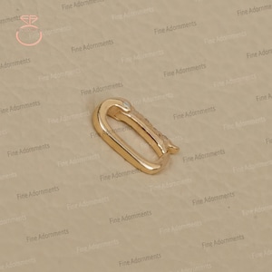 May include: A gold-colored, oval-shaped clasp with a hinged closure. The clasp is made of a shiny metal and has a small, decorative element on the side. The background is a neutral beige color.