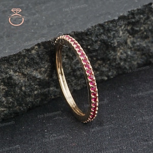 May include: A thin gold band ring with a row of small, bright red gemstones.
