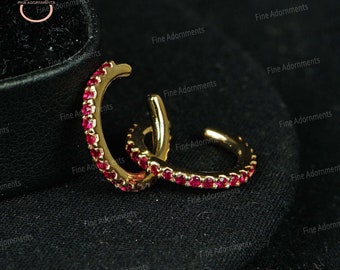 May include: A pair of gold hoop earrings with a row of small, red gemstones around the edge.
