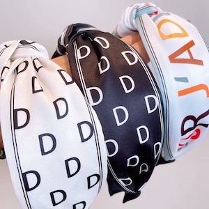 May include: Three fabric headbands with different patterns. One headband is white with black letter D's, another is black with white letter D's, and the third is white with the word "JADE" in colourful letters.