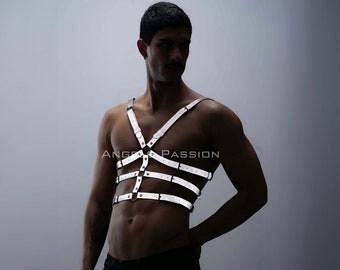 May include: A white leather harness with silver accents. The harness has multiple straps that crisscross the chest and back. The harness is worn by a person with a dark complexion and short black hair.