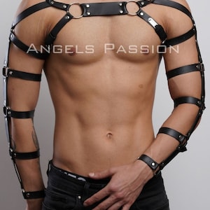 May include: Black leather body harness with metal ring accents and arm cuffs. The harness features straps across the chest and shoulders, with additional straps around the upper arms and forearms. The text "ANGELS PASSION" is visible on the chest.