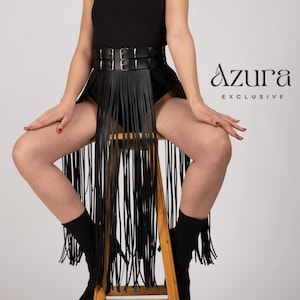 May include: A black leather fringe skirt with a double-buckle belt. The skirt is paired with a black top and boots. The Azura Exclusive logo is visible in the image.
