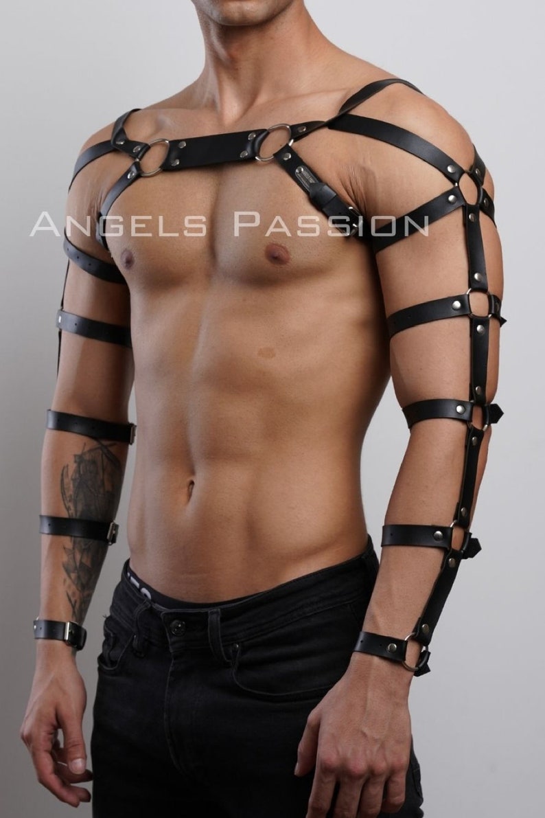 May include: Black leather body harness with metal rings and buckles. The harness features straps across the chest, shoulders, and arms. The text "ANGELS PASSION" is visible in the image.
