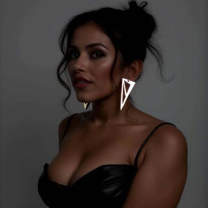 May include: A woman wearing large, geometric, triangle-shaped earrings. The earrings are a bright, reflective silver color. She is wearing a black, strappy top. Her hair is pulled back in a bun.