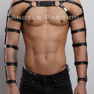 May include: Black leather body harness with shoulder straps, armbands, and wrist cuffs. The harness features metal rings and buckles. The text "ANGELS PASSION" is printed on the chest area. The product is designed for fashion or fetish wear.
