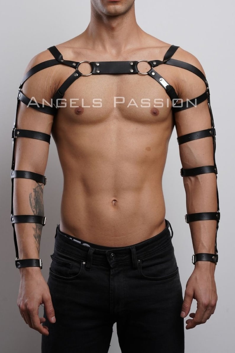 May include: Black leather body harness with shoulder straps, armbands, and wrist cuffs. The harness features metal rings and buckles. The text "ANGELS PASSION" is printed on the chest area. The product is designed for fashion or fetish wear.