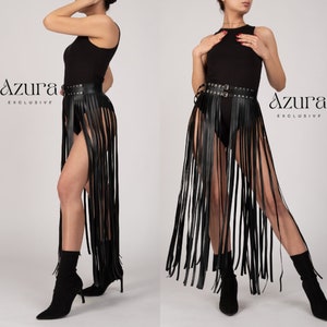 Puede incluir: Falda negra con flecos de cuero y cinturón con tachuelas. La falda tiene flecos largos y verticales y un cinturón de doble hebilla. El logo Azura Exclusive es visible. La falda se usa con un body y botas negras.