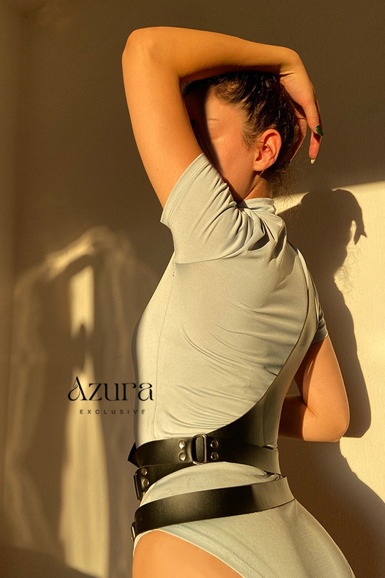Puede incluir: Un body gris claro con cuello alto y mangas cortas. Un cintur&oacute;n ancho de cuero negro con hebillas plateadas se lleva en la cintura. La imagen incluye el texto "Azura Exclusive".