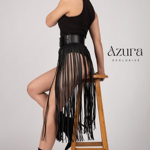May include: Black leather fringe skirt with a wide belt and double buckle closure. The skirt is paired with a black top and black heeled boots. The Azura Exclusive logo is visible on the right side.