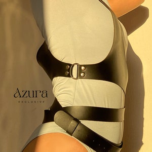 Puede incluir: Arn&eacute;s de cuerpo de cuero negro con hebilla y detalle de cintur&oacute;n, usado sobre un body gris claro. La imagen incluye el texto "AZURA EXCLUSIVE".