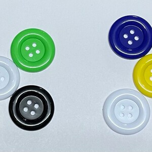 May include: Assortment of colourful plastic buttons with four holes each. The buttons are in various colours, including purple, green, yellow, white, black, and blue.