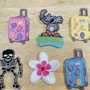May include: A set of ten iron-on patches featuring a variety of designs, including a skeleton, a koala, a flower, and suitcases. The patches are colourful and feature a variety of textures.